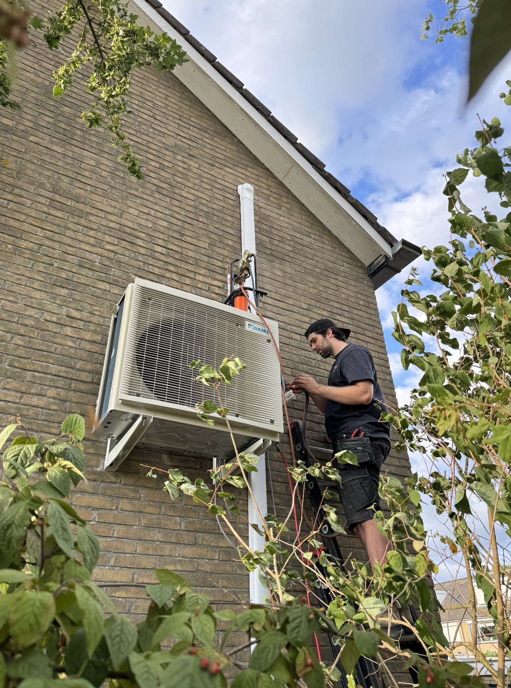WTV-monteur monteert een airco-buitenunit aan de gevel